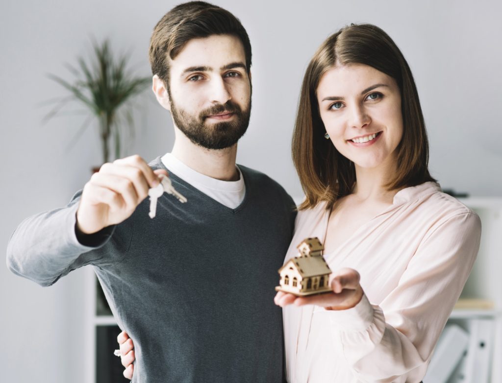 A couple holding a model house and keys to their new home.