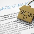A gold key with a house on top of a mortgage loan agreement.