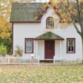 A white house in the fall with a white picket fence.